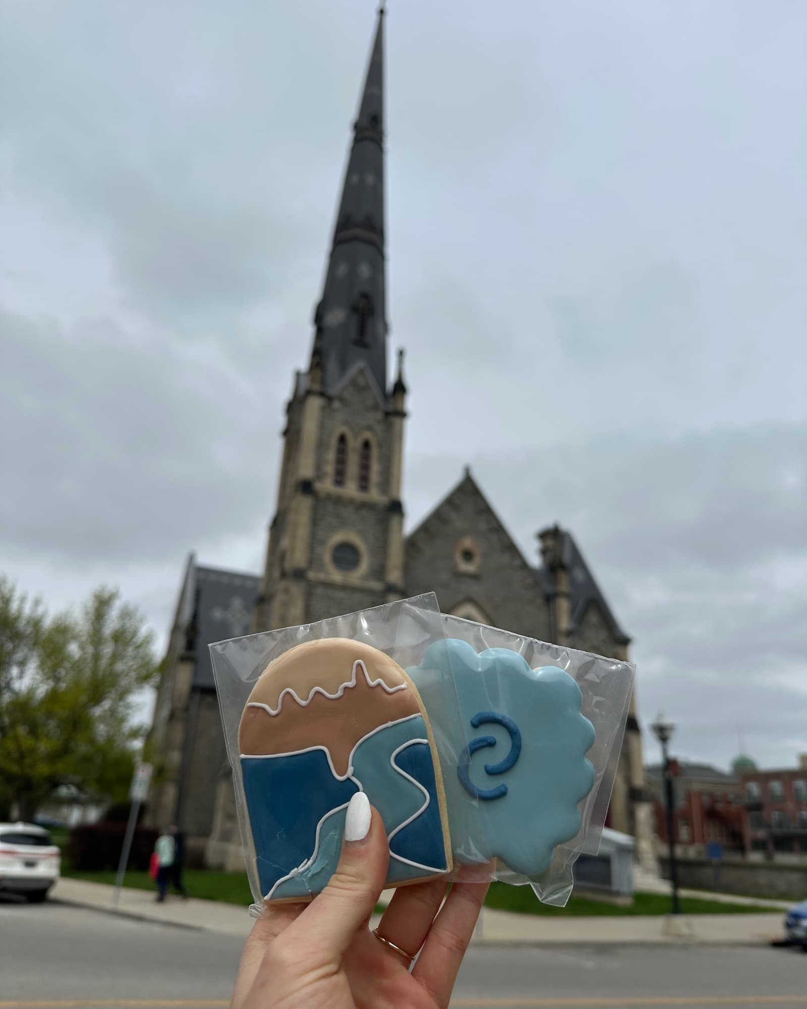 Hand holding two Clarity branded iced cookies against a stone church backdrop in Cambridge