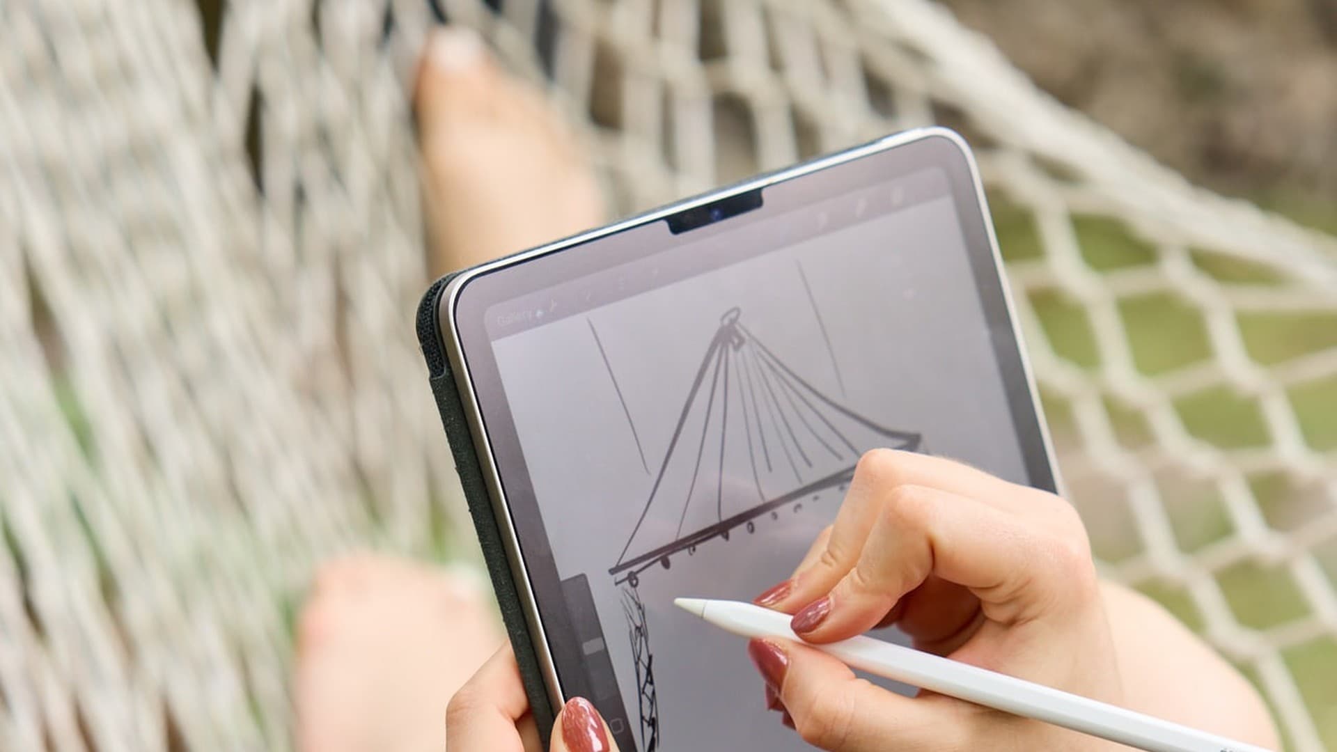 Hands drawing on a tablet while seated in a hammock outdoors.