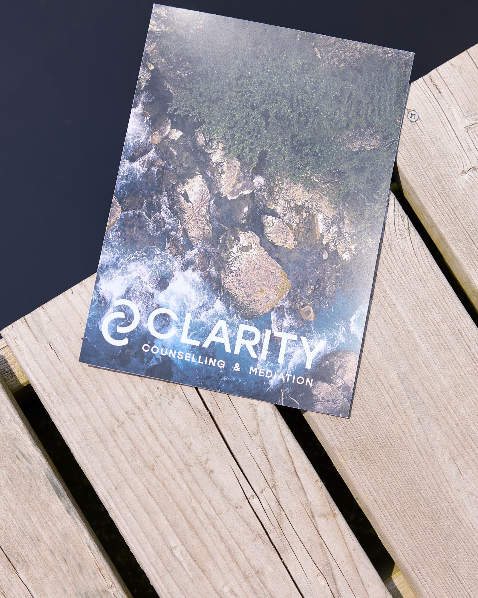 Printed Clarity Counselling and Mediation card with wave imagery on a weathered wooden dock