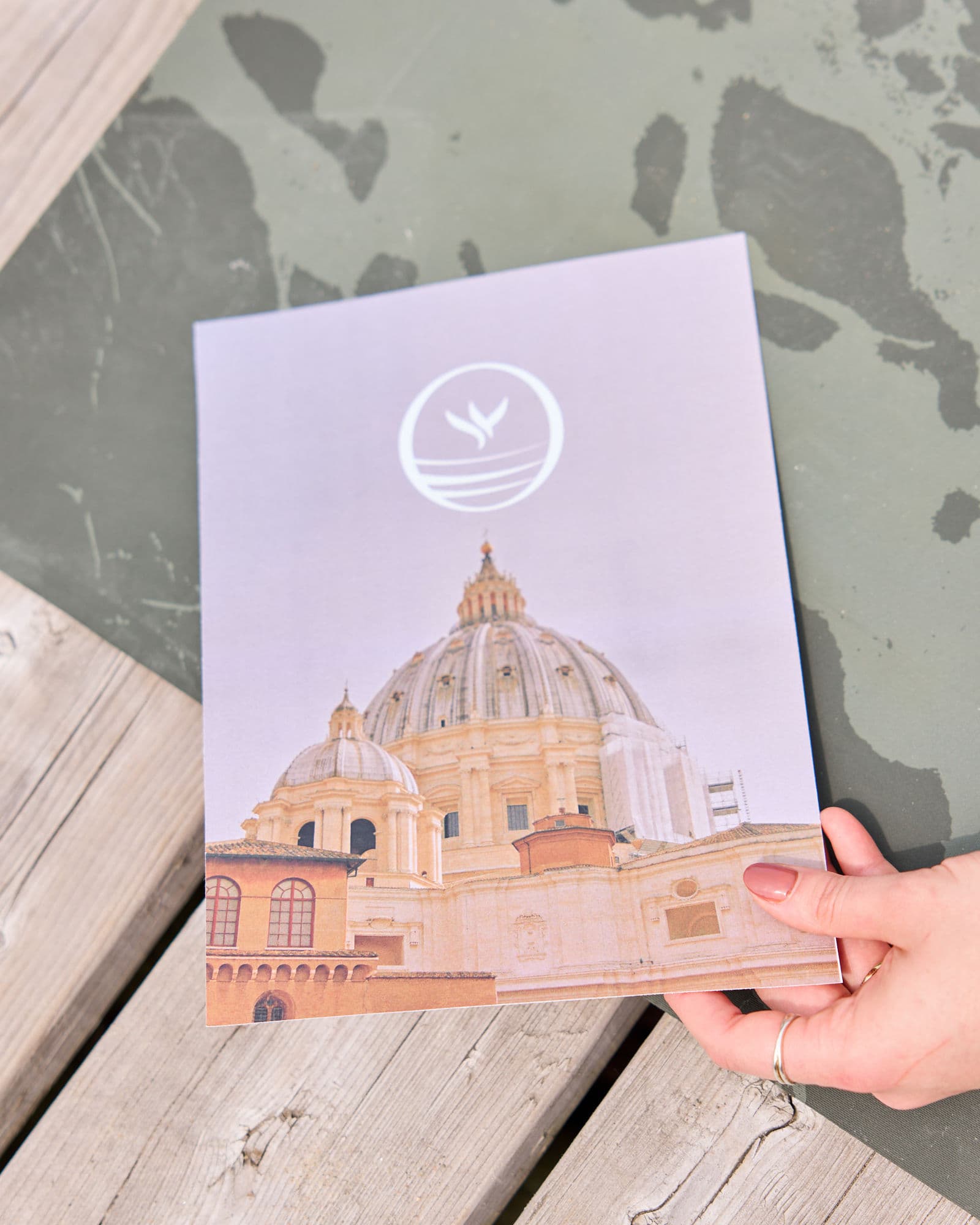 Hand holding a Rada Flow card with bird and wave stamp over classical architecture photography